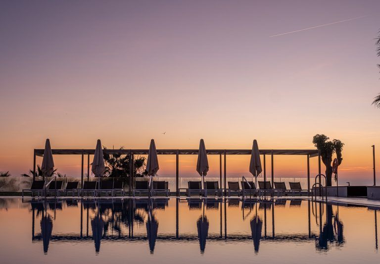 Sombrillas y hamacas al amanecer reflejadas en la piscina del hotel Torrequebrada en Málaga